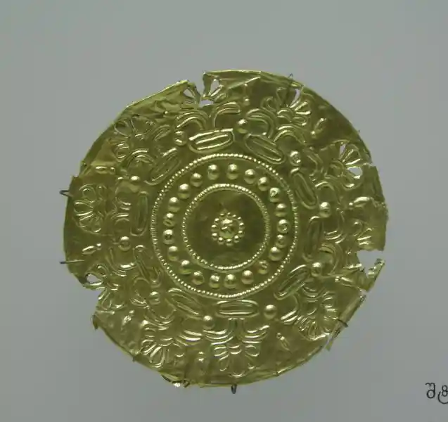 Gold circular plaque with sun at the center and horn-like half-sun cross around the circle
